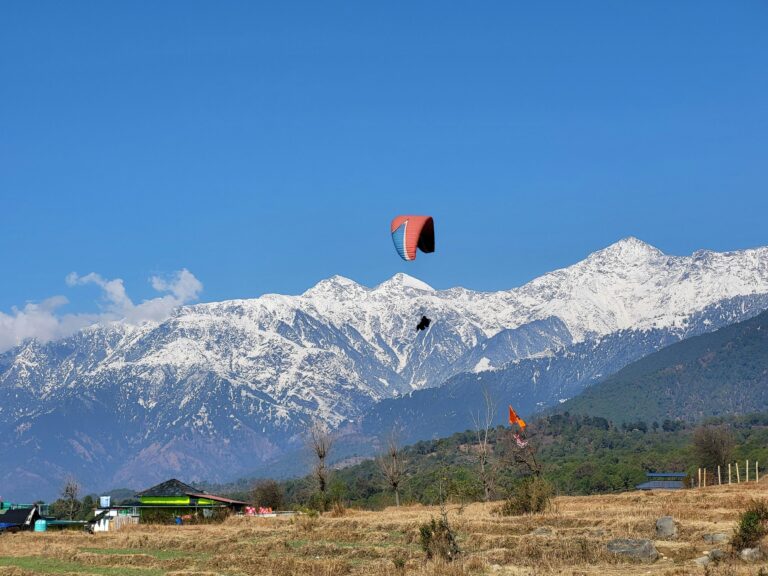 Home Paragliding adventure over the scenic snowy mountains of Bir, India, under a clear blue sky.